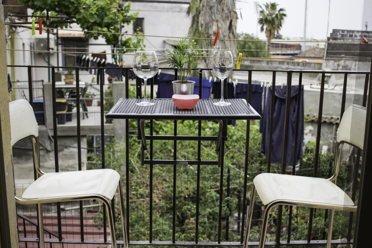 A small table and two chairs on the balcony, with neighbouring buildings beyond the railing.